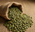 Fresh green pumpkin seeds spilling from a burlap sack on rustic fabric, natural healthy snack